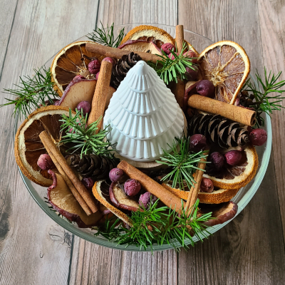 A glass bowl of handcrafted holiday potpourri with a small white fir-shaped essential oil passive diffuser on a wood tabletop