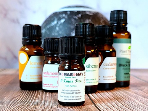 A bottle of O Xmas Tree essential oil blend, bottles of ingredient essential oils, black ultrasonic diffuser