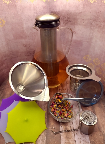 Herbal tea-making supplies, including tea infusers, fresh herbs, a tea kettle, tea steeping lids, and a reusable coffee filter.