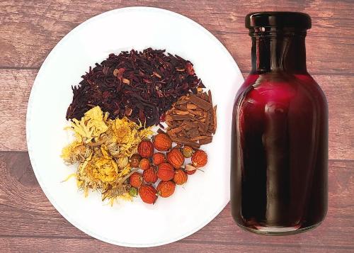 A bottle of Happy Hibiscus and Cinnamon Red Hair Rinse with plate of herb ingredients